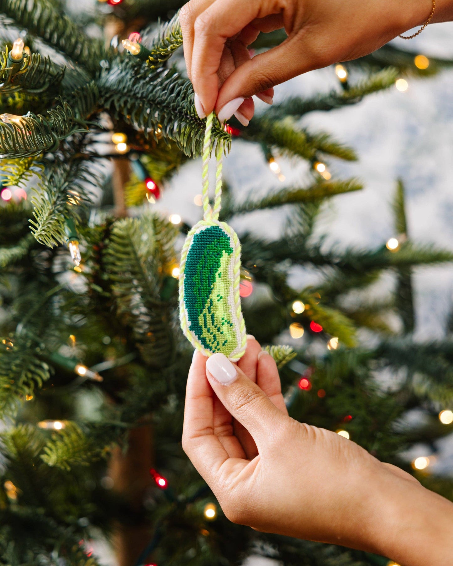 Hand holding a green embroidered ornament against a Christmas tree background