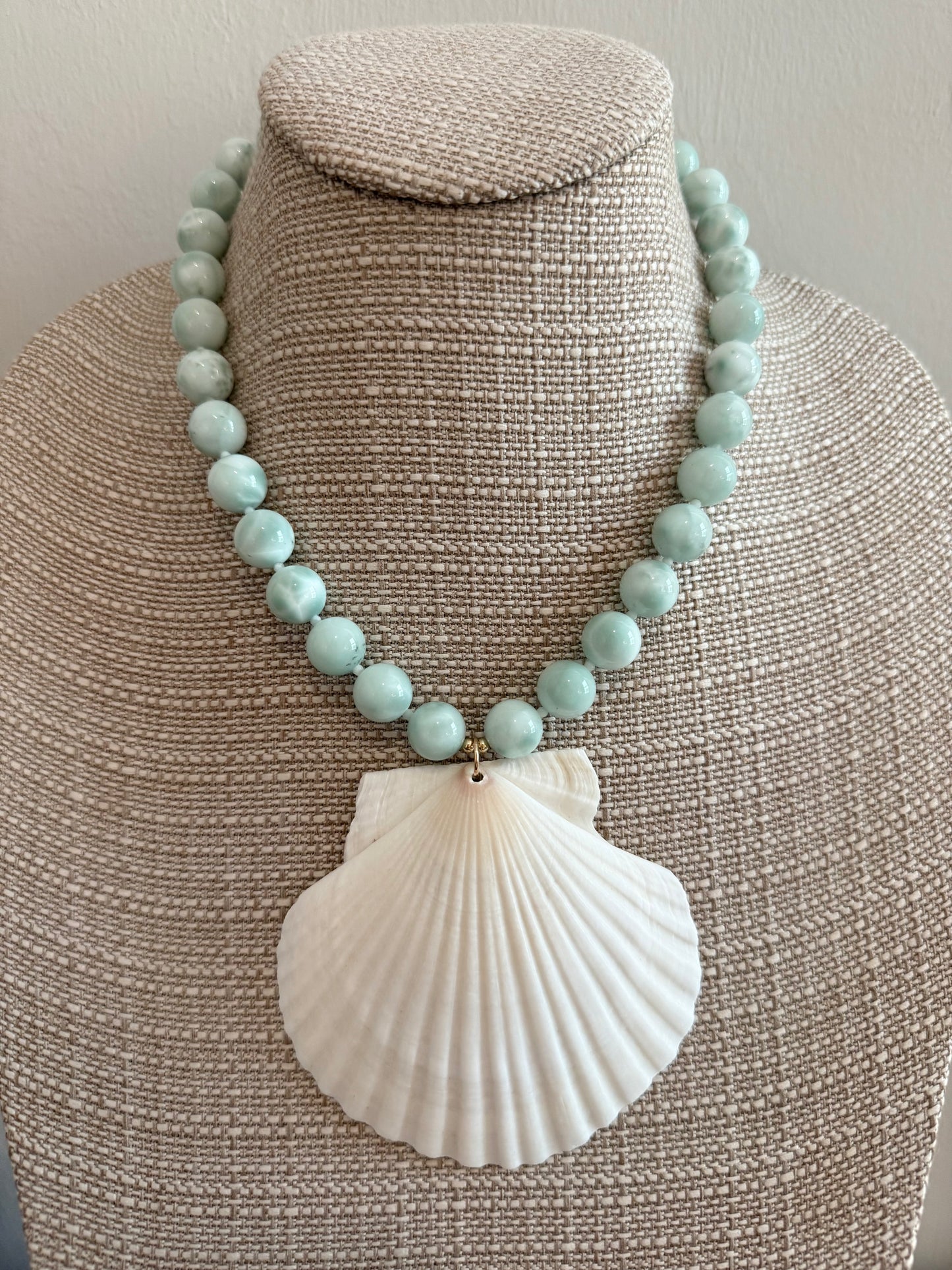 Necklace with turquoise beads and a large white shell pendant on a mannequin bust.