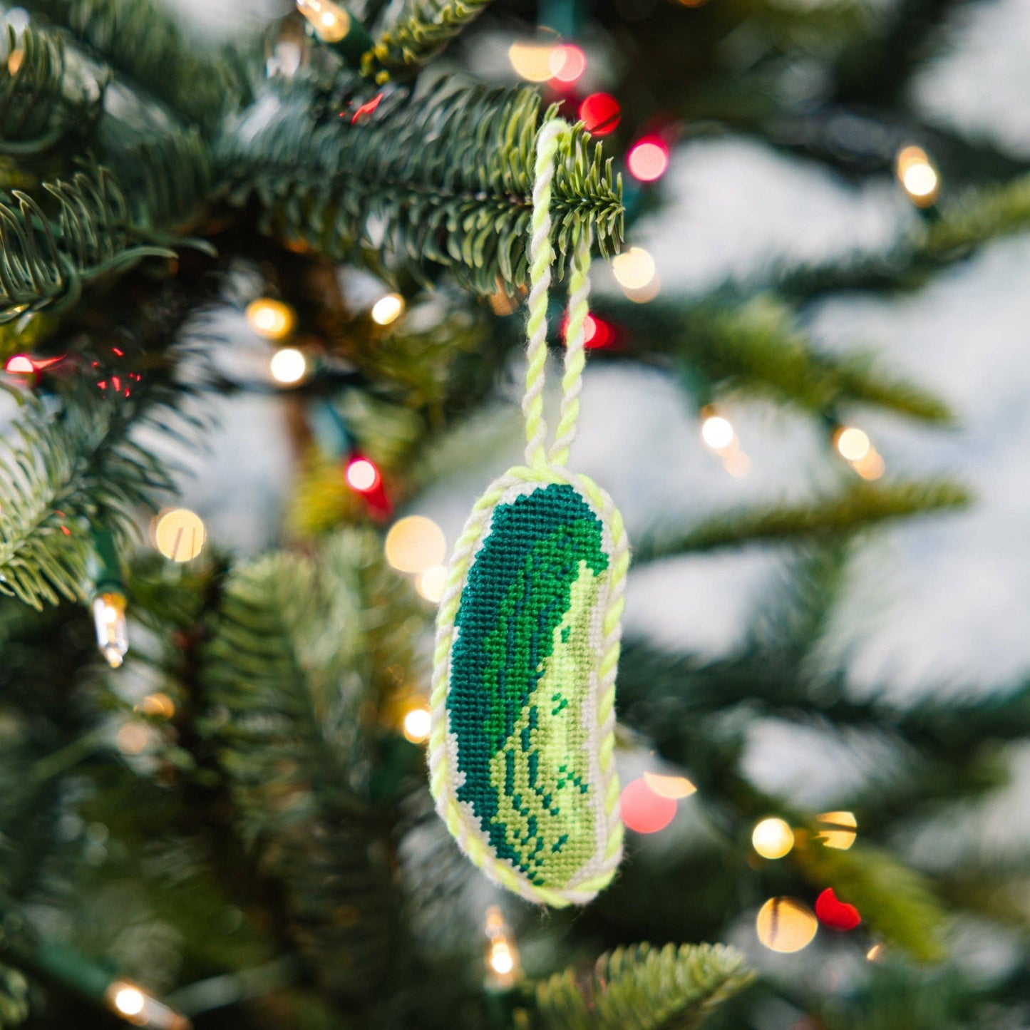 Decorative pickle ornament hanging on a Christmas tree with blurred lights in the background