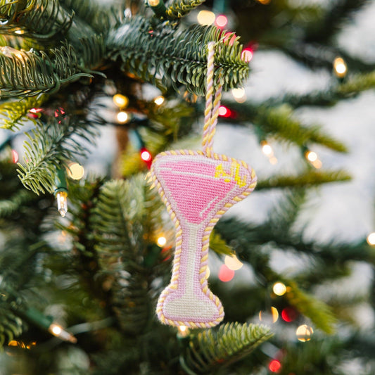 Decorative cocktail glass ornament hanging on a Christmas tree with lights in the background