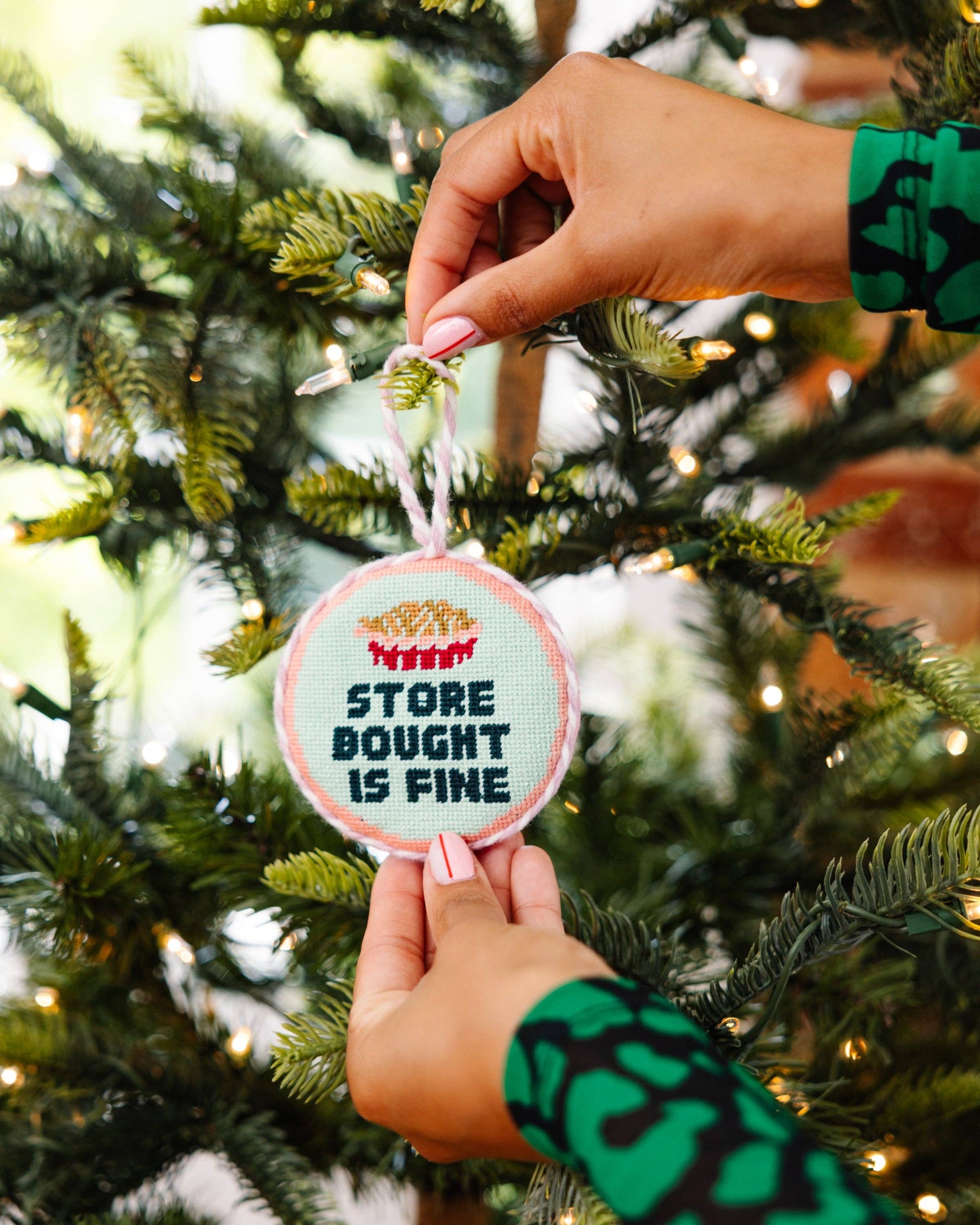 Hand holding a Christmas ornament with text on a decorated tree