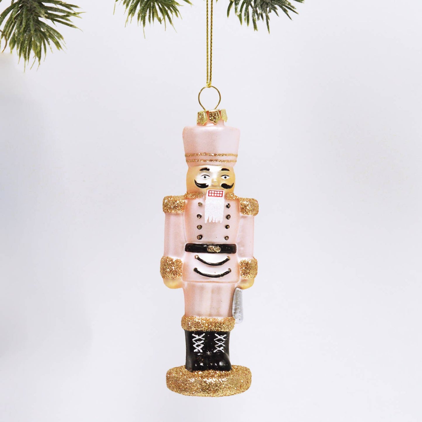 Christmas ornament shaped like a nutcracker with pink body and gold accents on a white background.
