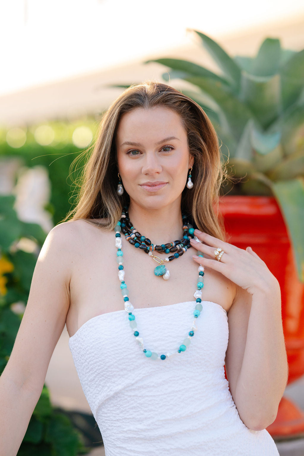 Woman wearing a white dress and multiple necklaces with a blurred outdoor background