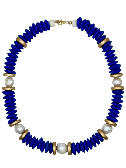 Necklace with blue beads, gold accents, and pearls on a beige fabric background