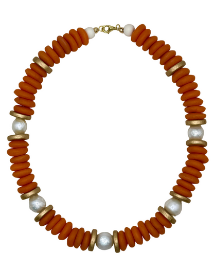 Necklace with orange beads, gold accents, and pearls on a light fabric background
