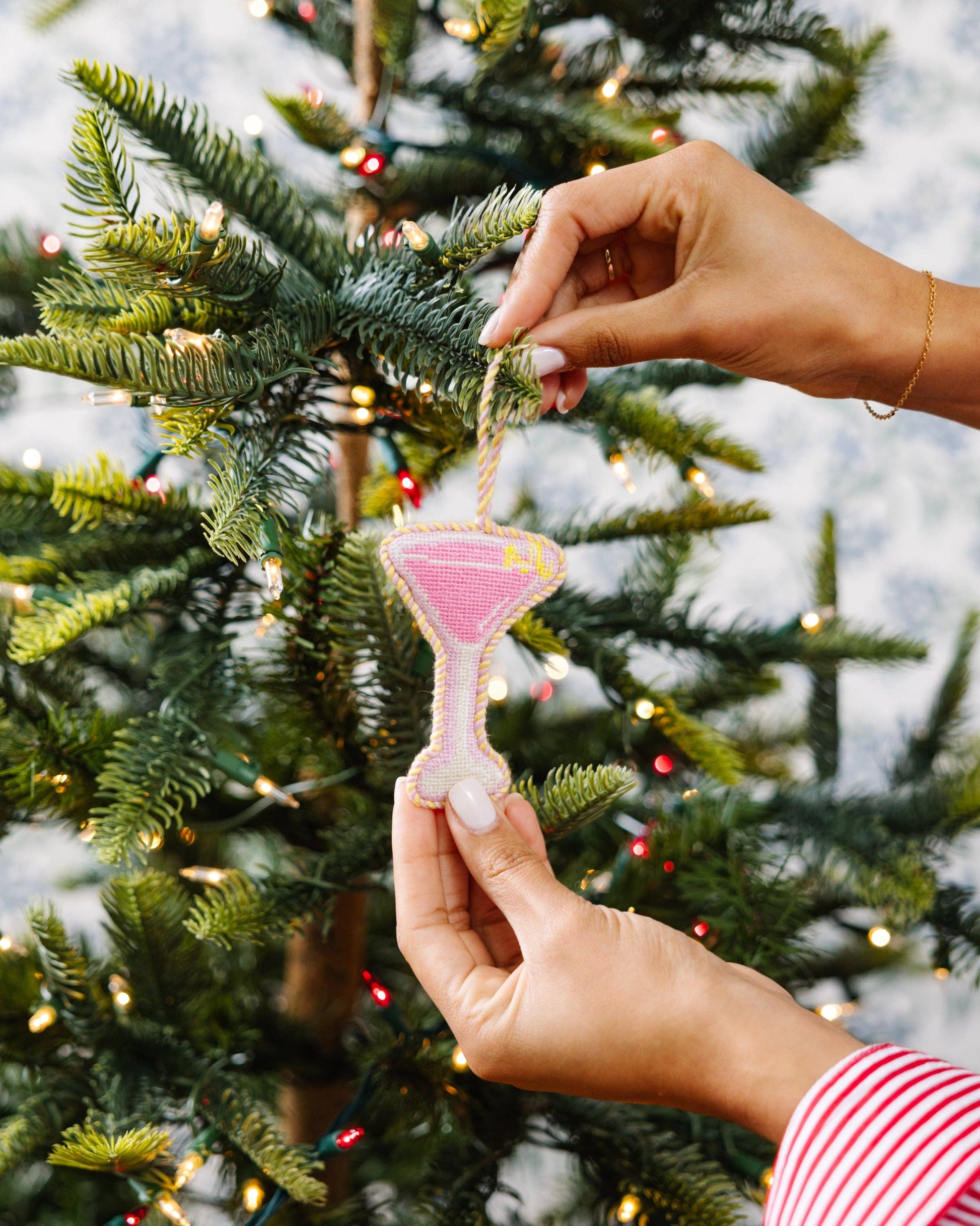 Person holding a pink ornament against a Christmas tree background