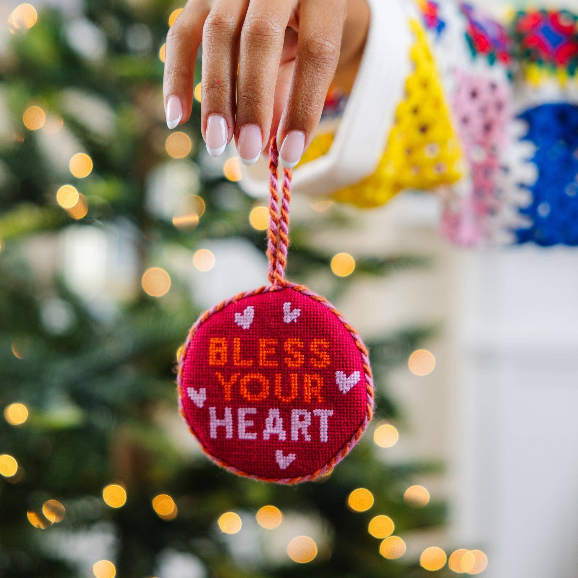 Decorative ornament with 'Bless Your Heart' text held by a hand against a festive background.