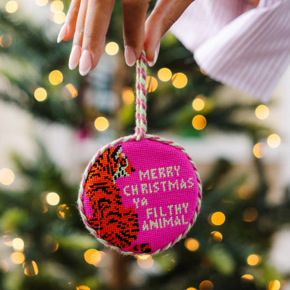 Decorative Christmas ornament with tiger design and text, held against a festive background.